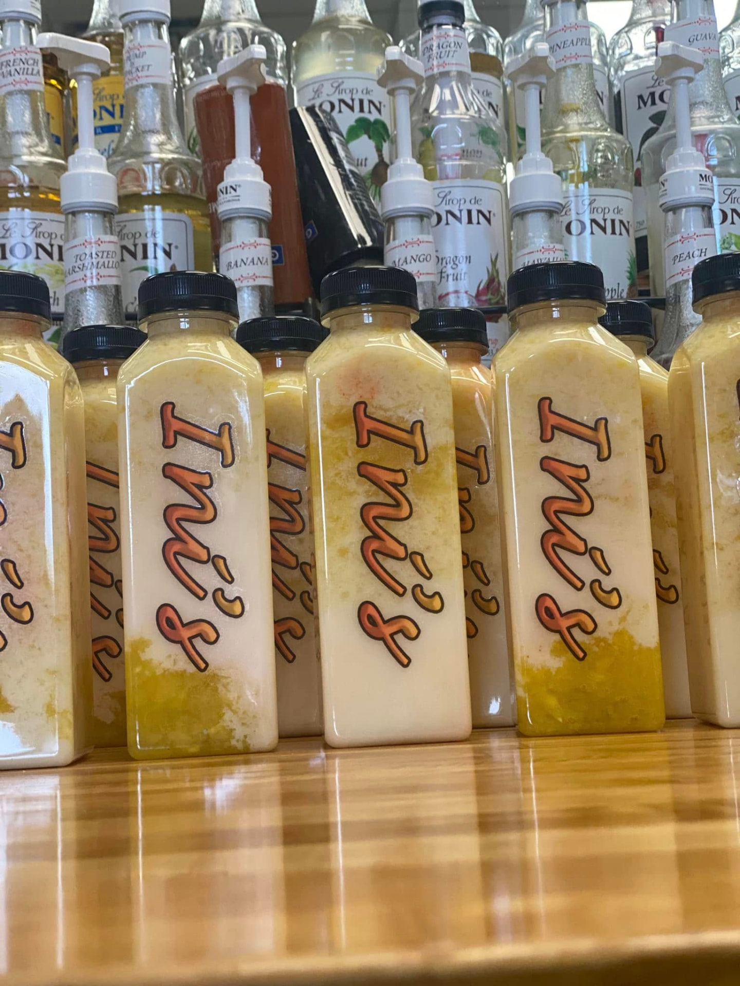 Bottled Ini's drinks lined up on the oak counter beneath the syrup wall